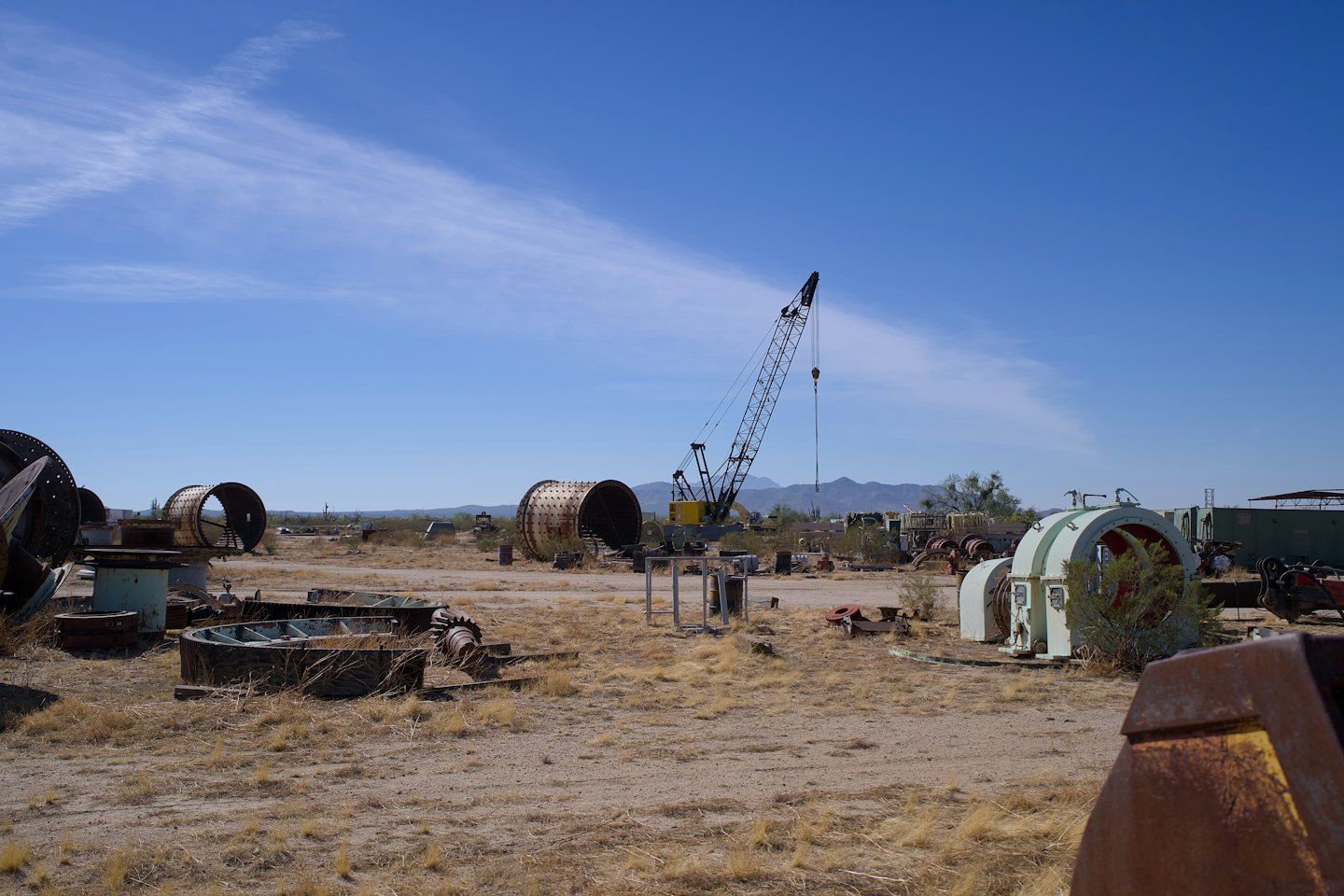 Salvage yard with rusted industrial machinery and a crane.