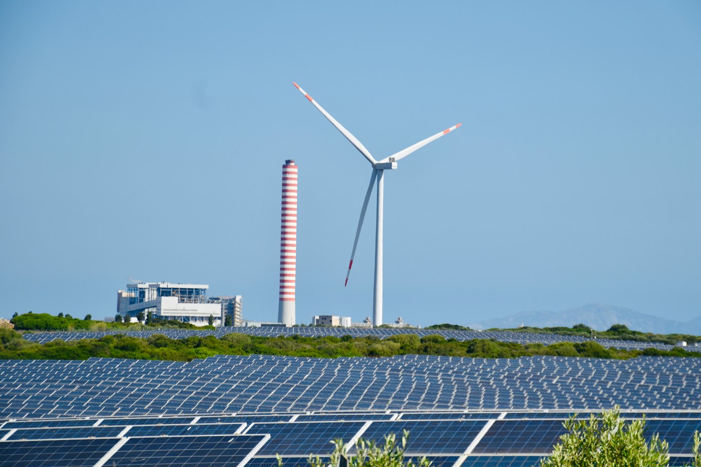 Solar panels in a field with a building and wind turbine.